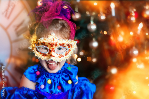 Portrait of funny laughing 4 years old girl in carnival venetian mask. Christmas tree, big clock on background. Christmas lights. Space for text. Happy and funny christmas and new year in childhood