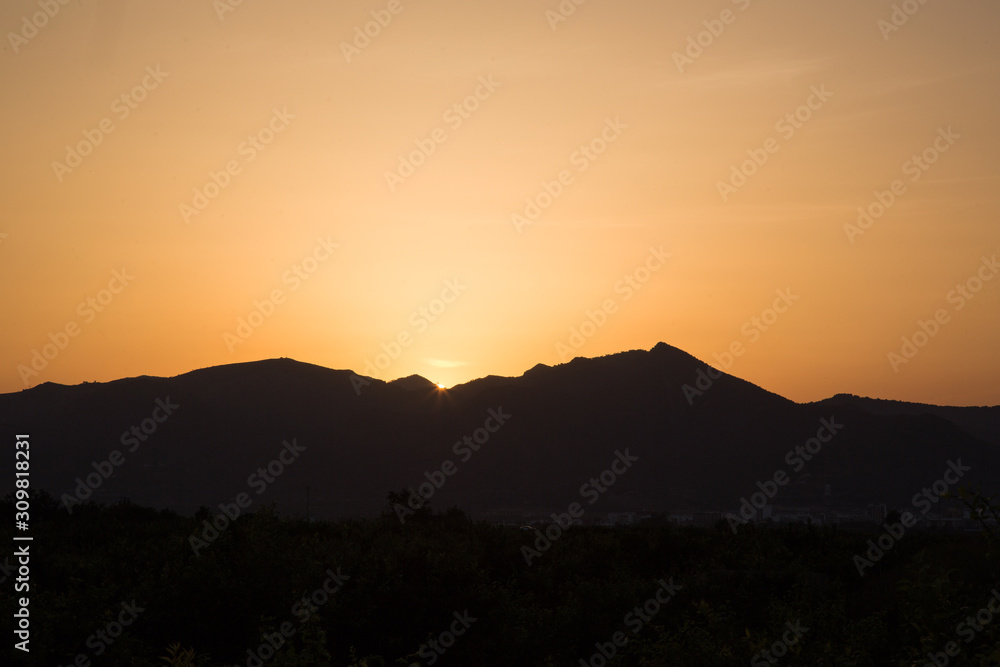 Beautiful sunset. Magical landscape. The sun sets behind the dark silhouettes of mountains. Yellow sunset sky.
