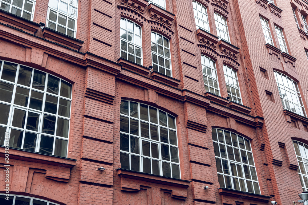 The facade of a classic red brick building with large windows. Brick architecture of a prestigious area. Expensive real estate.