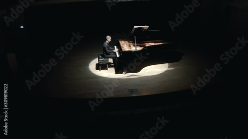 Grand Piano On Stage : An elegant man in a black suit playing grand piano on stage in a concert hall, aerial video