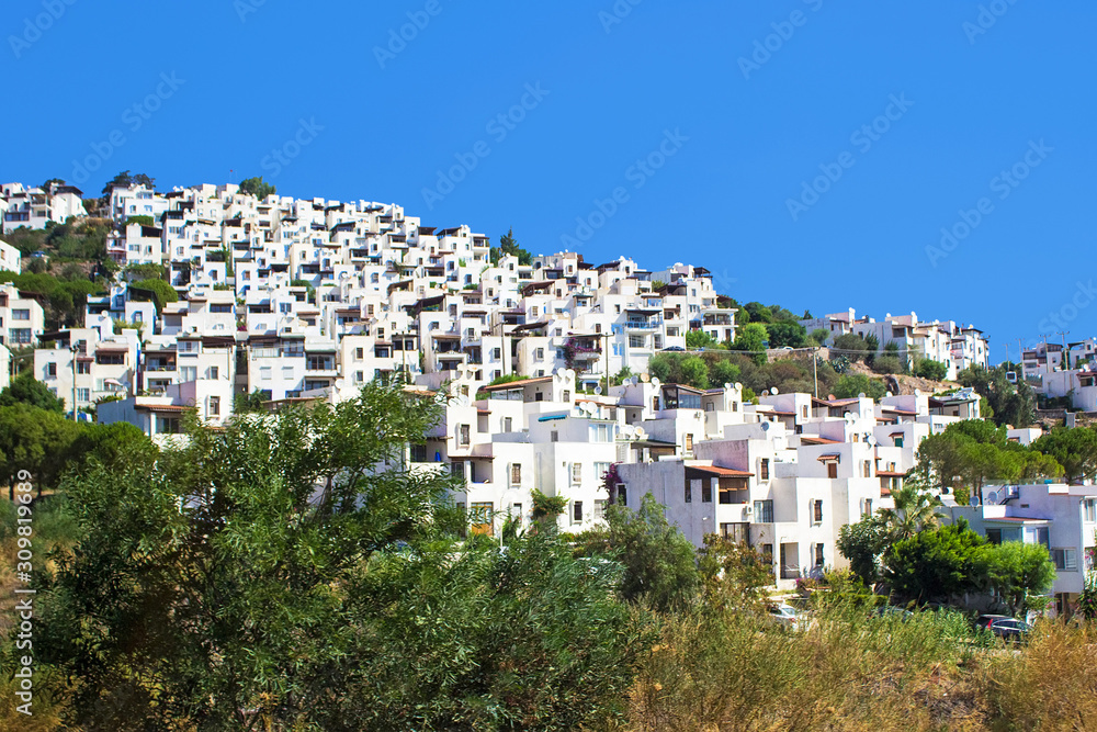 Panoramic view on Bodrum downtown with traditional white cubic buildings, green trees and mountains on background. Aegean style, Bodrum town, Mugla, Turkey.