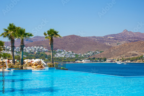Beautiful view on turquoise Water Pool, white deck chairs, palms and deep blue Aegean sea near luxury Turkish hotel, Akyarlar region of Bodrum, Turkey. Turkish vacation. photo