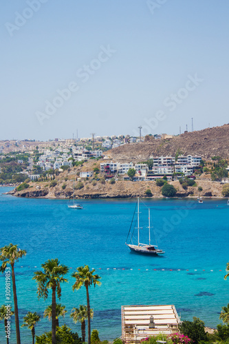 Fototapeta Naklejka Na Ścianę i Meble -  Beautiful view on turquoise  Aegean sea with yacht and pontoon that moored on the seashore with sunbeds and umbrellas near luxury Turkish hotel in Akyarlar region of Bodrum, Turkey. Turkish vacation.