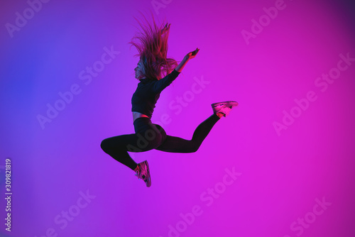 Sporty charismatic woman jumping against colorful trendy color. Young athletic girl in jump moment in studio
