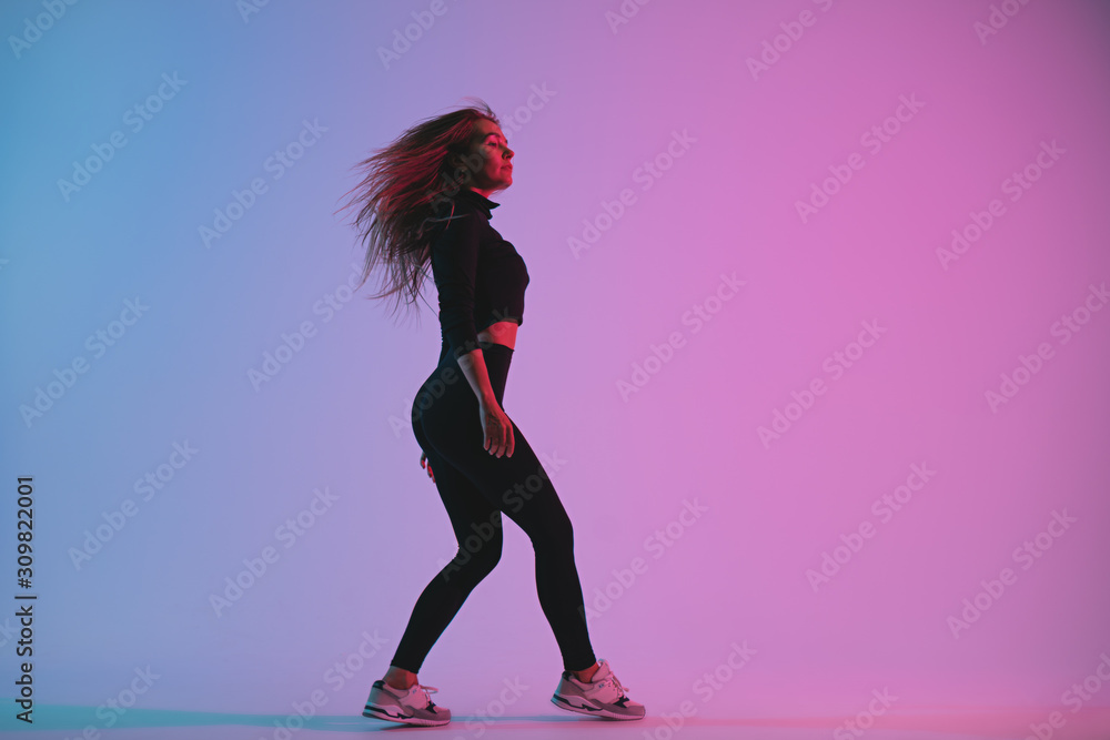 Handsome woman with perfect body dancing in studio against colorful trendy color. Beautiful athletic girl posing in fitness clothing
