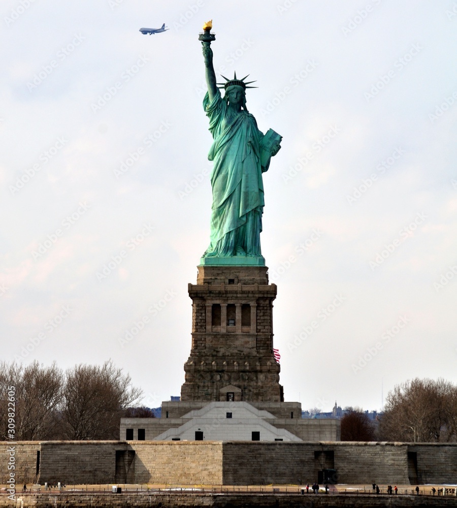 Obraz premium The Statue of Liberty view from water with passenger plane on background