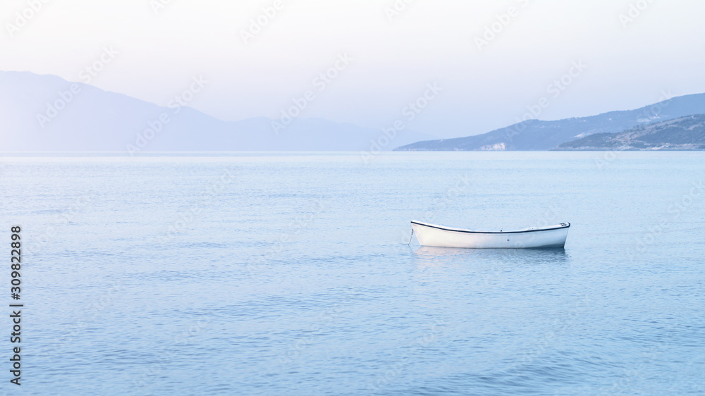 Tender shades of pastel blue morning haze color sunrise with white boat at anchor in blue waters. Travel and vacation destination concept or peace and tranquility concept banner with copy space
