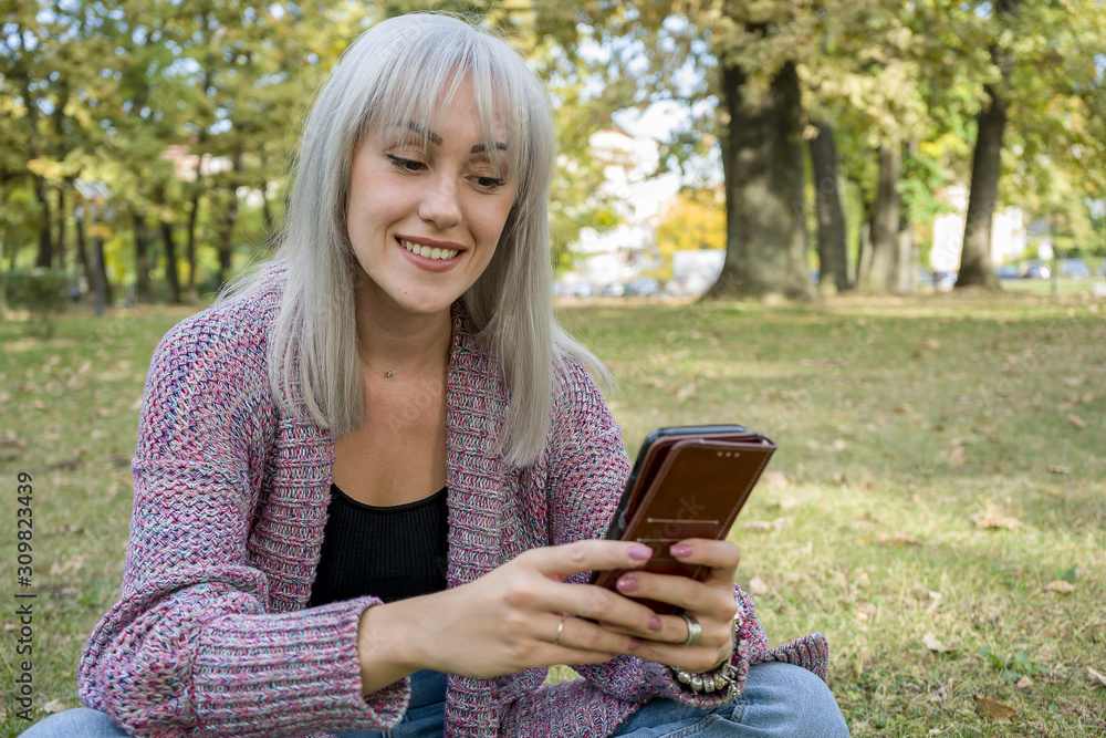 Obraz premium Outdoors portrait of a woman looking at the phone. Silver hair.