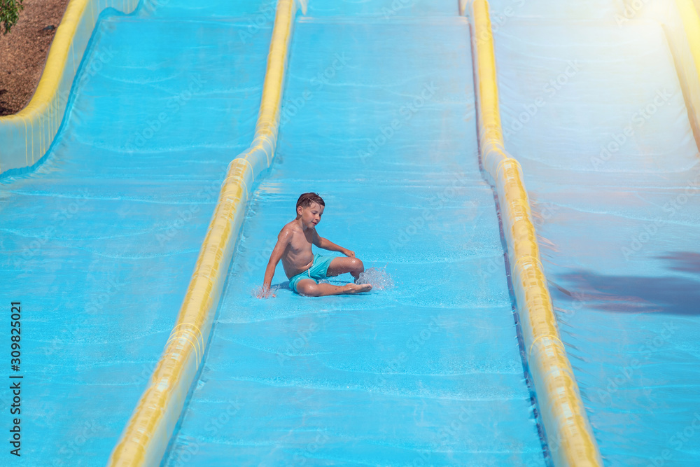 Active Caucasian boy in water park in Spain. He sliding down colorful waterslide and enjoying summer vacations.