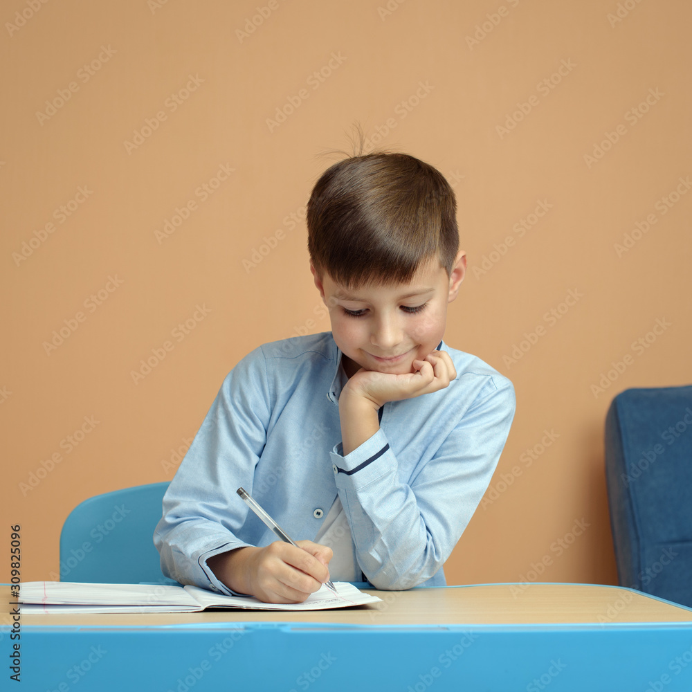 Cheerful Caucasian schoolboy in uniform doing task at classroom. First time to school. Back to school. Cheerful Caucasian schoolboy in uniform doing task at classroom. First time to school. Back to school.