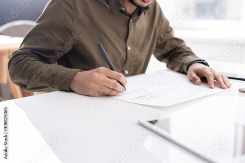 Young busy economist drawing flow chart on paper while preparing report