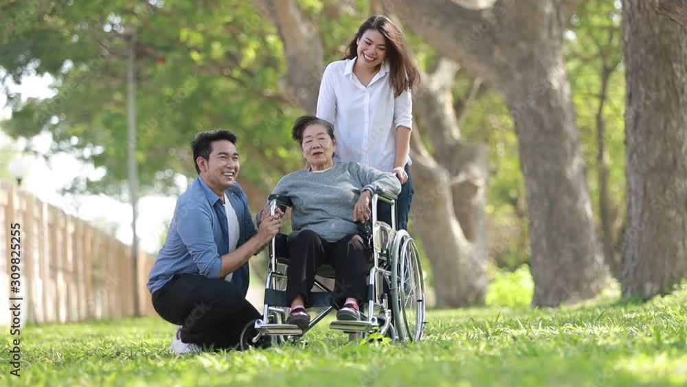 Asian woman sitting on wheelchair in the park with family Asian woman sitting on wheelchair in the park with family