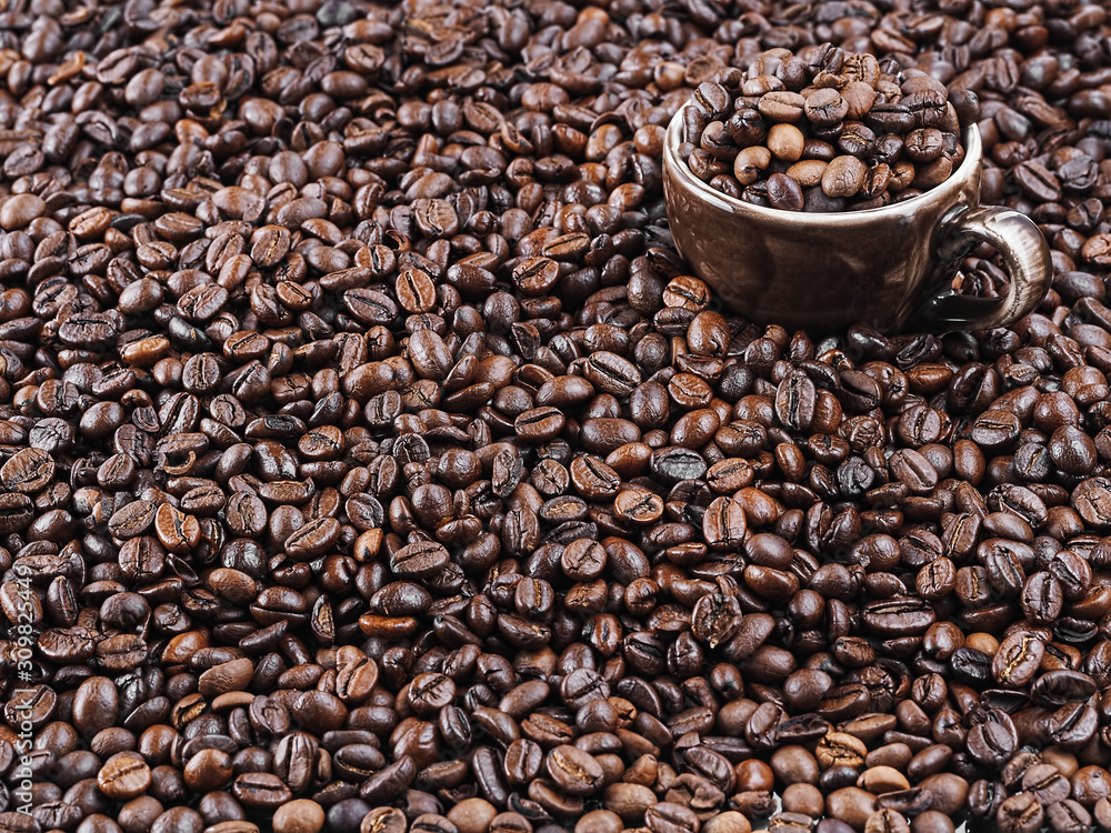 Fototapeta premium Roasted coffee beans, background. Horizontal orientation. Fresh aromatic dark coffee. A brown cup for espresso stands in coffee beans. Close-up. Selective focus on a cup with coffee grains.
