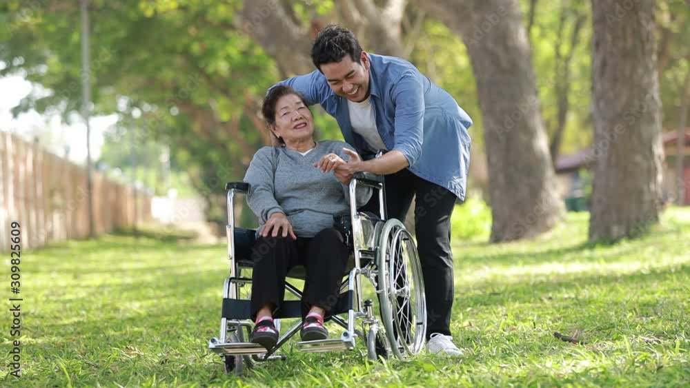 Asian woman sitting on wheelchair in the park with family Asian woman sitting on wheelchair in the park with family