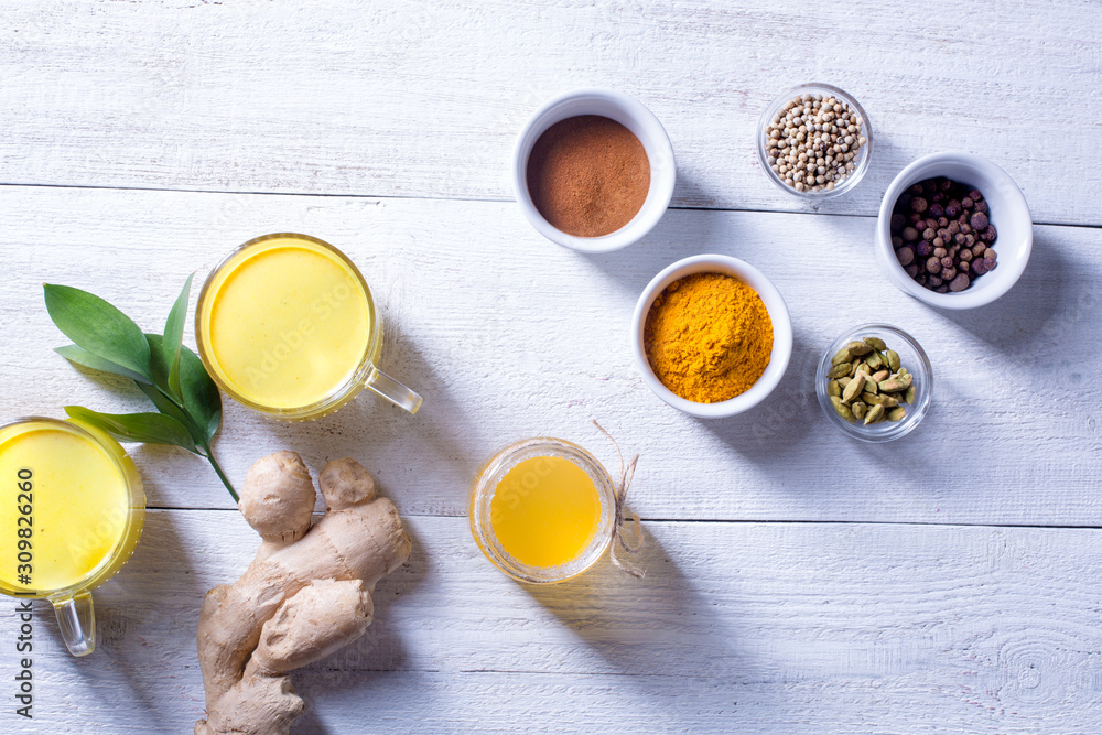 Turmeric Ginger tea. Two glass cups with golden latte, honey, turmeric, ginger root, cardamom and cinnamon on a white wooden background. Turmeric Ginger tea. Two glass cups with golden latte, honey, turmeric, ginger root, cardamom and cinnamon on a white wooden background.