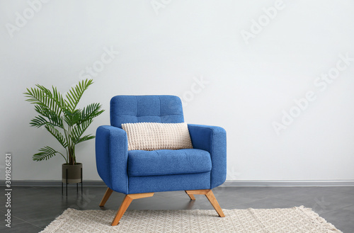Comfortable blue armchair and houseplant near light wall photo