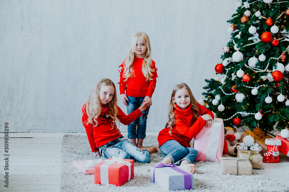 three small girls blonde in red dress at Christmas gifts new year holiday