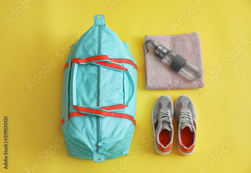 Gym bag and sports equipment on yellow background, flat lay