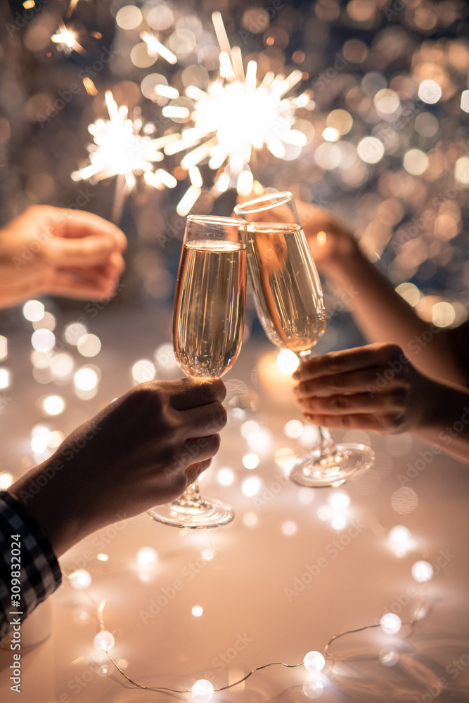 Hands of friends holding flutes of champagne and sparkling Bengal lights - obrazy, fototapety, plakaty 