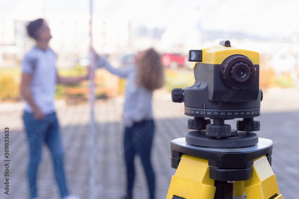 Two students of architecture doing practice lessons as Surveyor Engineering. Surveyor’s telescope at construction site for making contour plans of the land before startup construction work. Two students of architecture doing practice lessons as Surveyor Engineering. Surveyor’s telescope at construction site for making contour plans of the land before startup construction work.