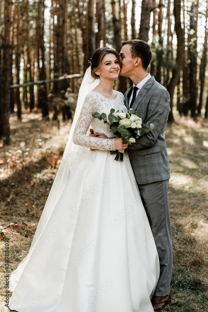 Attractive couple celebrating their wedding in forest. Portrait of young happy groom and bride in wedding clothes standing together, holding hands and looking at each other