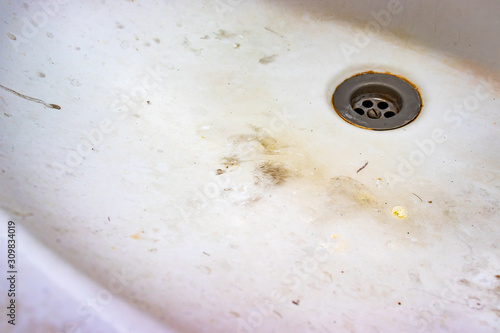 A sink drain hole with limescale or lime scale and rust on it, dirty rusty calcified bathroom washbowl with soap stains