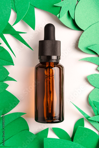 Glass bottle with aroma oil  paper green leaves on white background  aromatherapy concept healthcare minimal layout