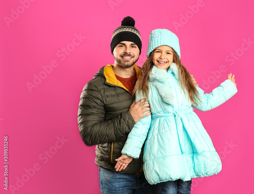 Happy father and daughter in warm clothes on pink background. Winter vacation