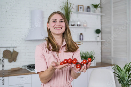 A smiling girl holds in her hands a beautiful branch of ripe cherry tomato.