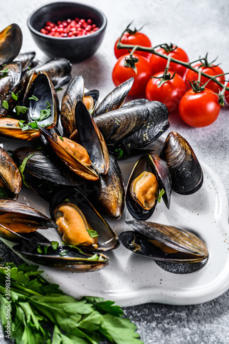 Fresh uncooked mussels in shells. The concept of cooking in tomato sauce with parsley. Gray background. Top view