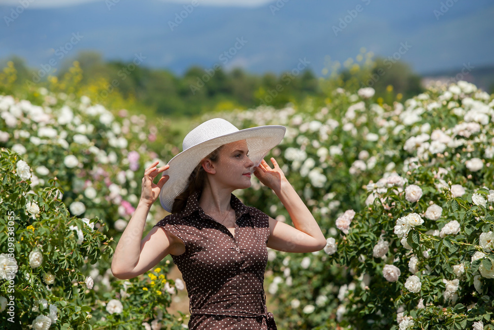 Beautiful woman in retro style polka dot dress and hat in Bulgarian rose garden.
