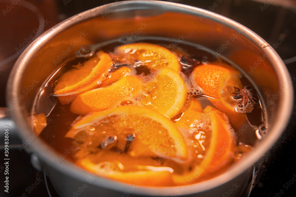 Making hot alcoholic mulled wine with oranges and spices. Christmas beverages boil in the metal pan. Glintwine from rose wine with citrus, cloves, star anise, cinnamon. Making hot alcoholic mulled wine with oranges and spices. Christmas beverages boil in the metal pan. Glintwine from rose wine with citrus, cloves, star anise, cinnamon.