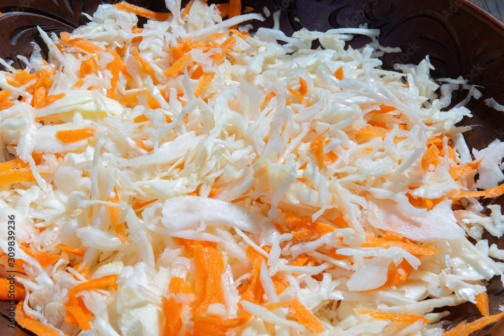 Fototapeta premium Grated cabbage and carrots in a ceramic bowl close-up