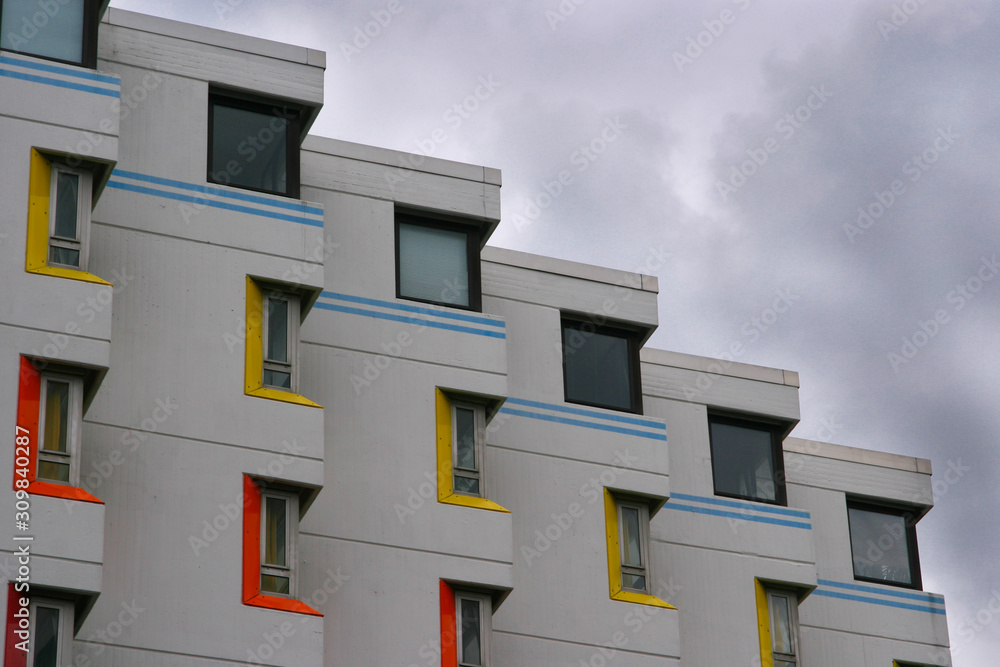 Detail of a facade of a residential building with red, yellow and blue details with moody sky in the background