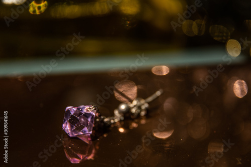 Purple jewel earring laying on a sparkly surface