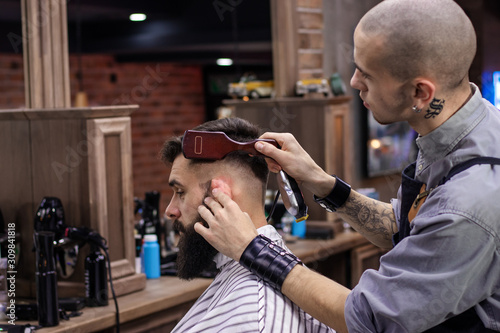 Hipster client during beard grooming and hairstyling in barber shop. Advertising and barber shop concept.