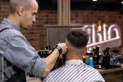 Getting perfect shape, hair styling and cutting with trimmer. Rear view of young bearded man getting haircut by hairdresser at barber shop. Advertising and barber shop concept.