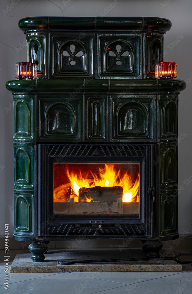 Naklejka premium Green antique tile stove. Fire burning in the fireplace. Candles on a tile stove. 