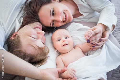 Top view happy positive Young family husband wife and little newborn baby lie on a cozy bed. Concept of a long-awaited child and child care