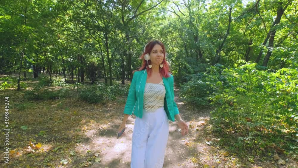 Young happy woman in colorful suit and with pink hair walk in summer park and listen to music Young happy woman in colorful suit and with pink hair walk in summer park and listen to music