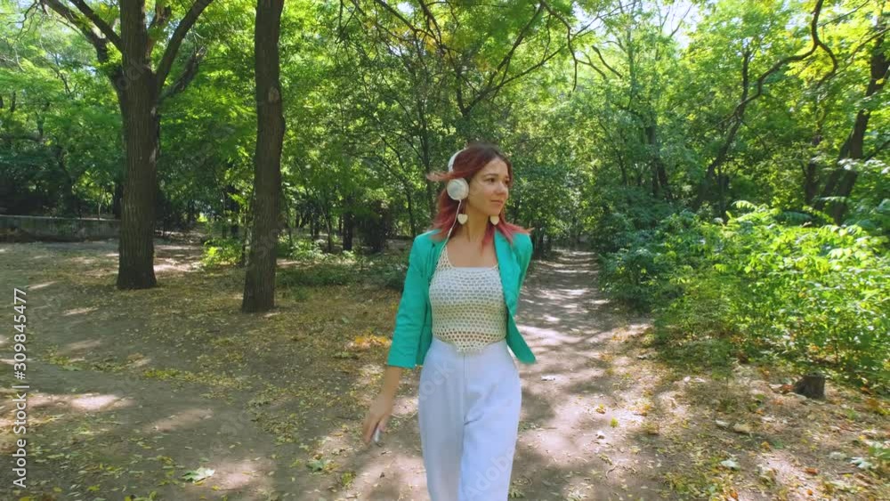 Young happy woman in colorful suit and with pink hair walk in summer park and listen to music Young happy woman in colorful suit and with pink hair walk in summer park and listen to music