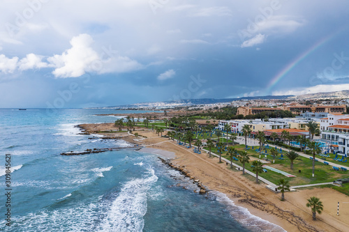 Paphos embankment or promenade, Cyprus, with sandy beach, green palm trees and lawns and small houses on first coastline, aerial view from drone. © DedMityay