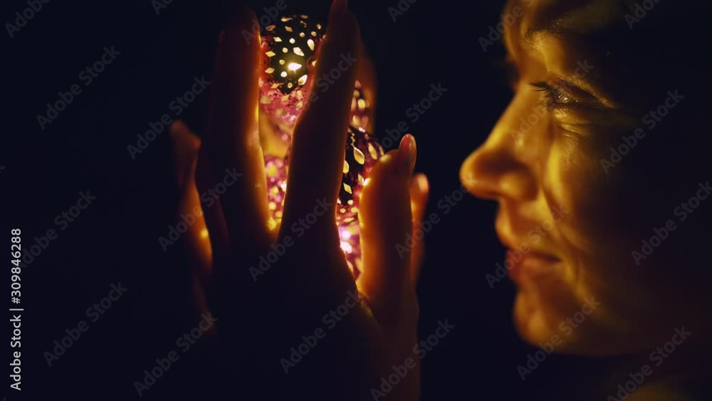 Magic hot light from lanterns falls on the woman eyes. The naked adult sexy caucasian girl lies at night on the bed and holds warm lamps in her hands. Christmas toy in black background. Indoor. Magic hot light from lanterns falls on the woman eyes. The naked adult sexy caucasian girl lies at night on the bed and holds warm lamps in her hands. Christmas toy in black background. Indoor.