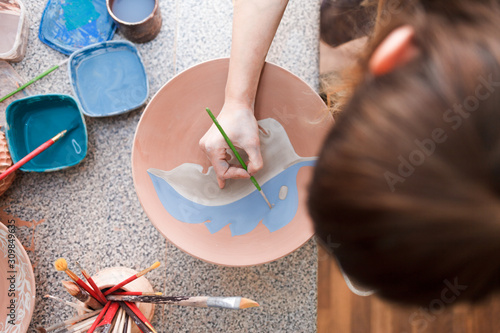 Potter woman paints a ceramic plate. Girl draws with a brush on earthenware. Process of creating clay products.  photo