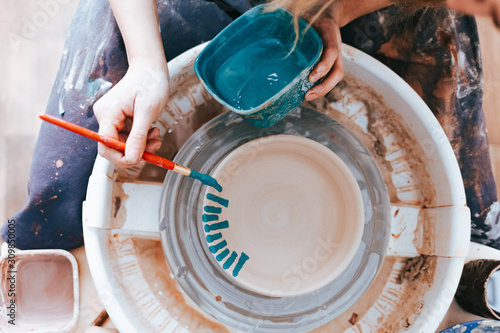 Professional potter works on painting plates in the workshop. Woman paints a ceramic plate with a brush and blue paint photo