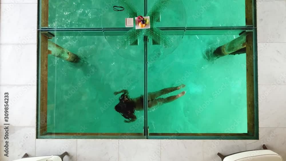 Aerial, top down, drone shot, of a girl, swimming under a villa, with a window floor, on the Conrad Rangali island, in Maldives Aerial, top down, drone shot, of a girl, swimming under a villa, with a window floor, on the Conrad Rangali island, in Maldives