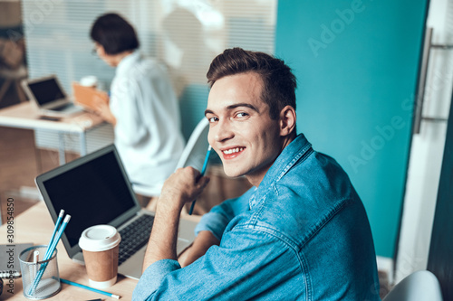 Smiling young man is looking at camera in office