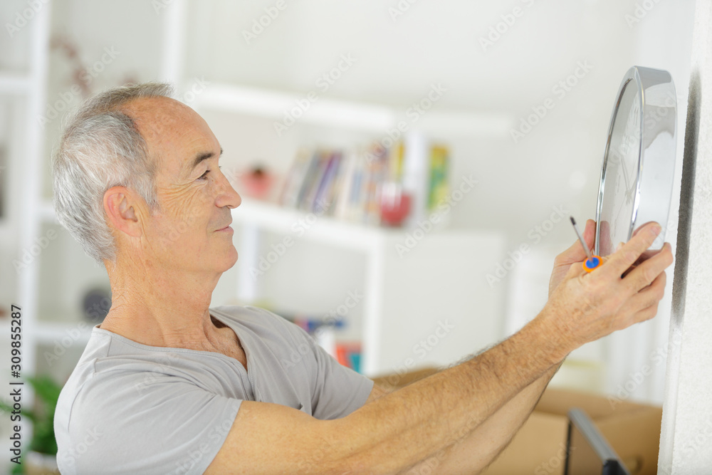 senior man putting a clock on the wall senior man putting a clock on the wall