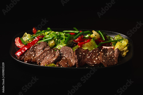 Juicy Beef Sirloin Steak Salad with bell pepper, sesam seeds and green vegetables in a black plate, on black background. Healthy food