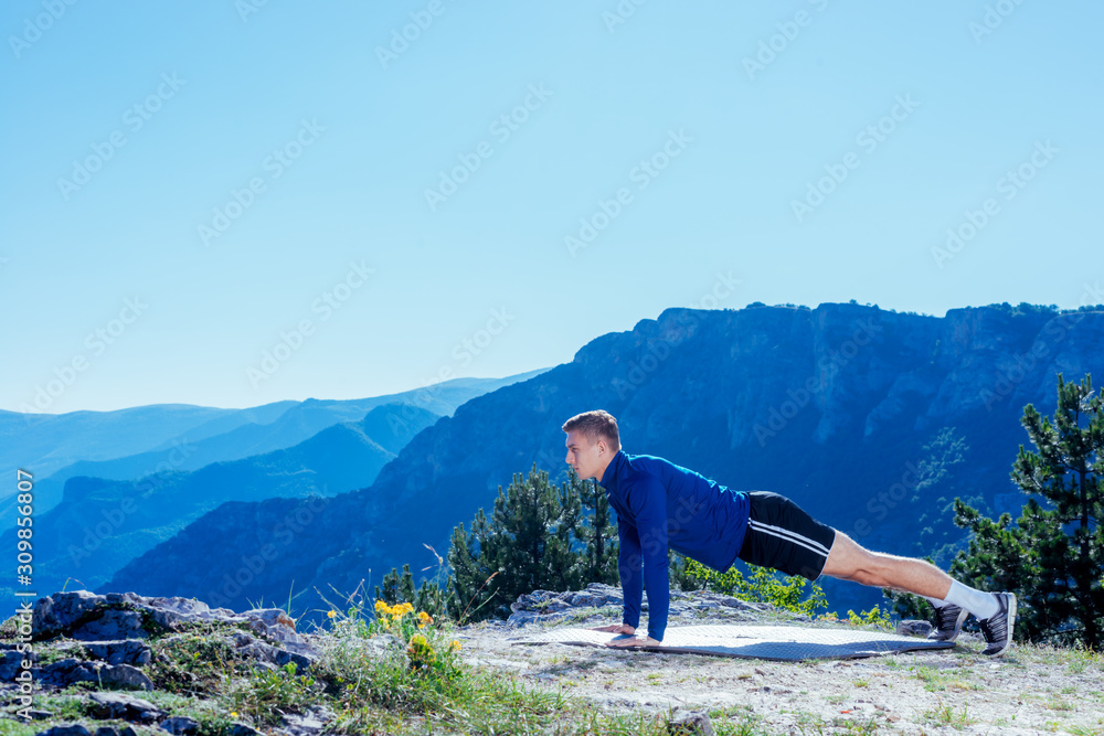 Strong handsome blonde athlete doing push ups on top of and mountain while enjoying the amazing view at the lake down in the valley.